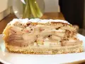 Pyszny kawałek szarlotki z warstwami jabłek i kremu, posypany cukrem pudrem. Idealna na deser.