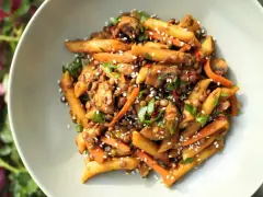 Sycący obiad bez mięsa: makaron penne z soczewicą, marchewką i pieczarkami, posypany sezamem i natką pietruszki.