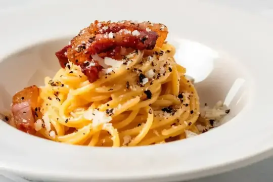 Spaghetti carbonara – przepis oryginalny ze śmietaną. Pyszne danie z makaronem, boczkiem i parmezanem, posypane świeżo mielonym pieprzem.