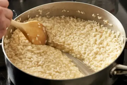 Drewniana łyżka miesza kremowy ryż do risotto w garnku, tworząc idealną konsystencję.