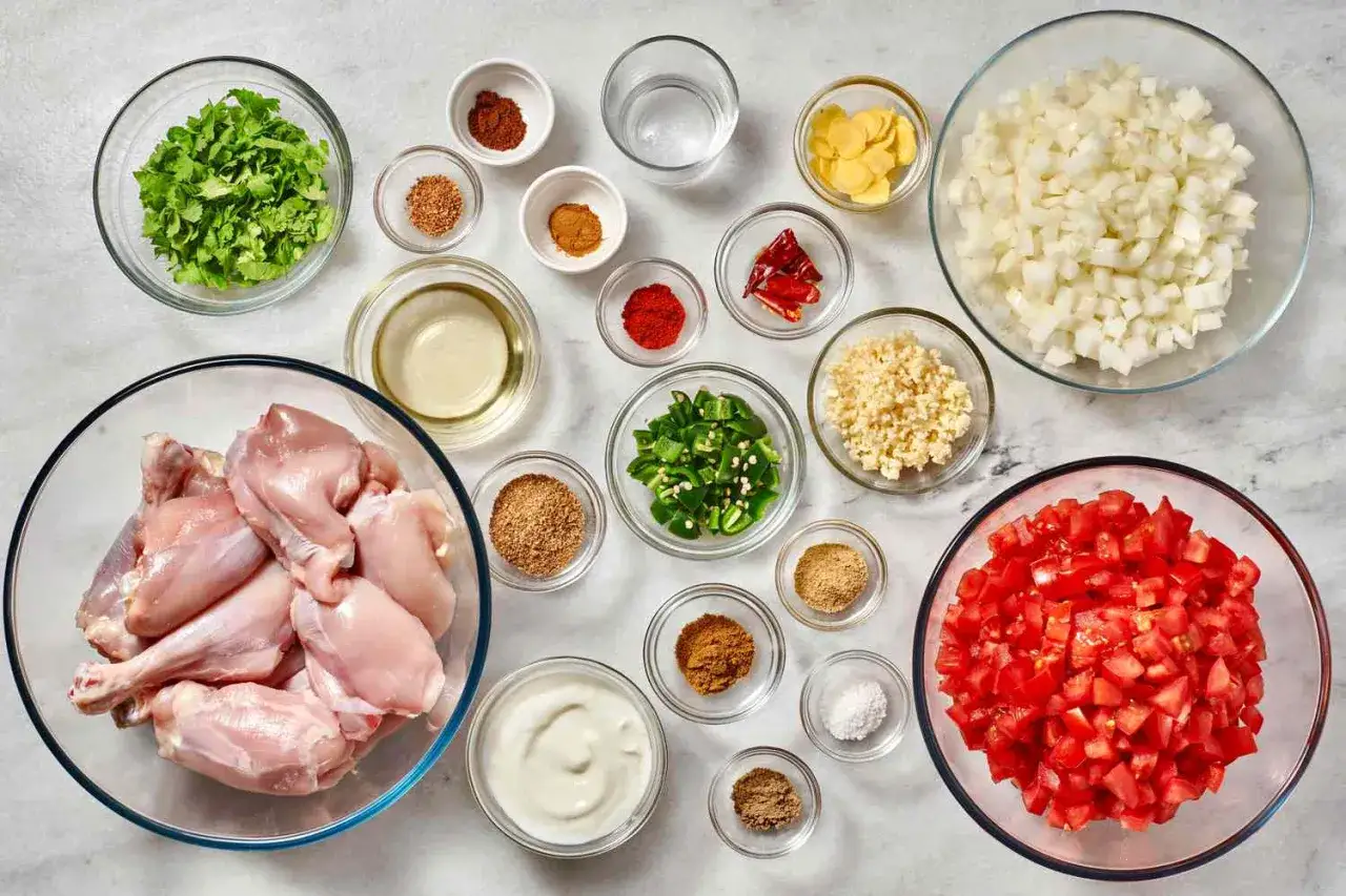 Składniki na kurczaka po indyjsku: surowy kurczak, pomidory, cebula, czosnek, imbir, papryczki chili, kolendra, jogurt i przyprawy.