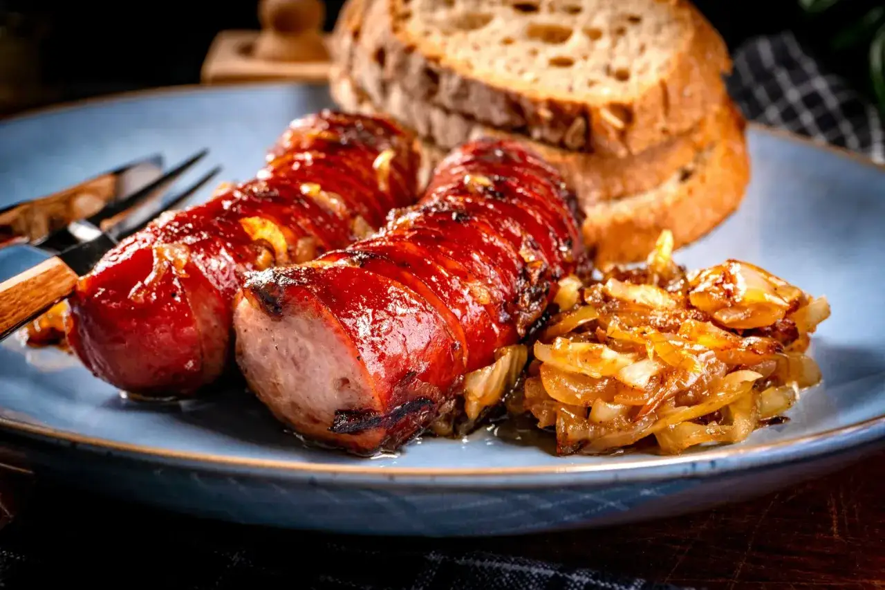 Pyszna kiełbasa z grilla, skropiona sokami, podana z karmelizowaną cebulką i chlebem. Idealna na letnie wieczory.