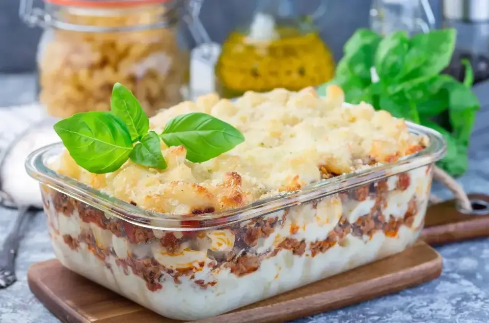 Zapiekanka makaronowa z mięsem mielonym w sosie śmietanowym, udekorowana bazylią, wygląda apetycznie.